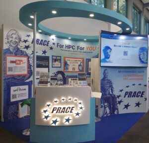 An ehibition booth with a blue circle above that holds canopy light, a curved counter decorated with a lighted PRACE logo, and a large TV on a wall on the right. The counter holds various signs and leaflets, and the back wall of the booth is decorated with project logos inside picture frames.