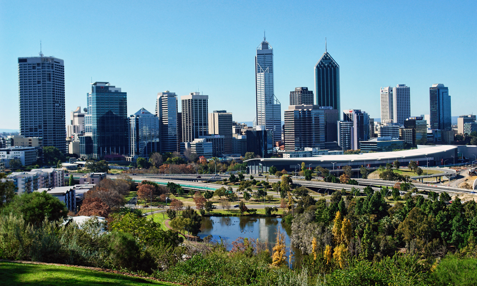 Skyline of Perth, Australia, with several skyscrapers in the background and a green park with a small lake in the foreground.