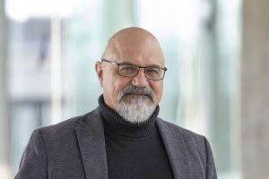 A portrait photo of Prof. Luciano Rezzolla, looking at the camera, wearing glasses and a grey beard.